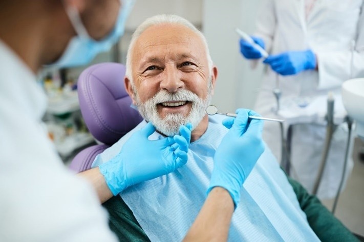 Smiling elderly man undergoing a dental checkup while a dentist uses tools to examine his teeth in a modern clinic.