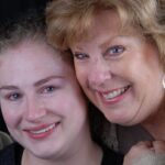 Two women smiling closely together showing healthy teeth.