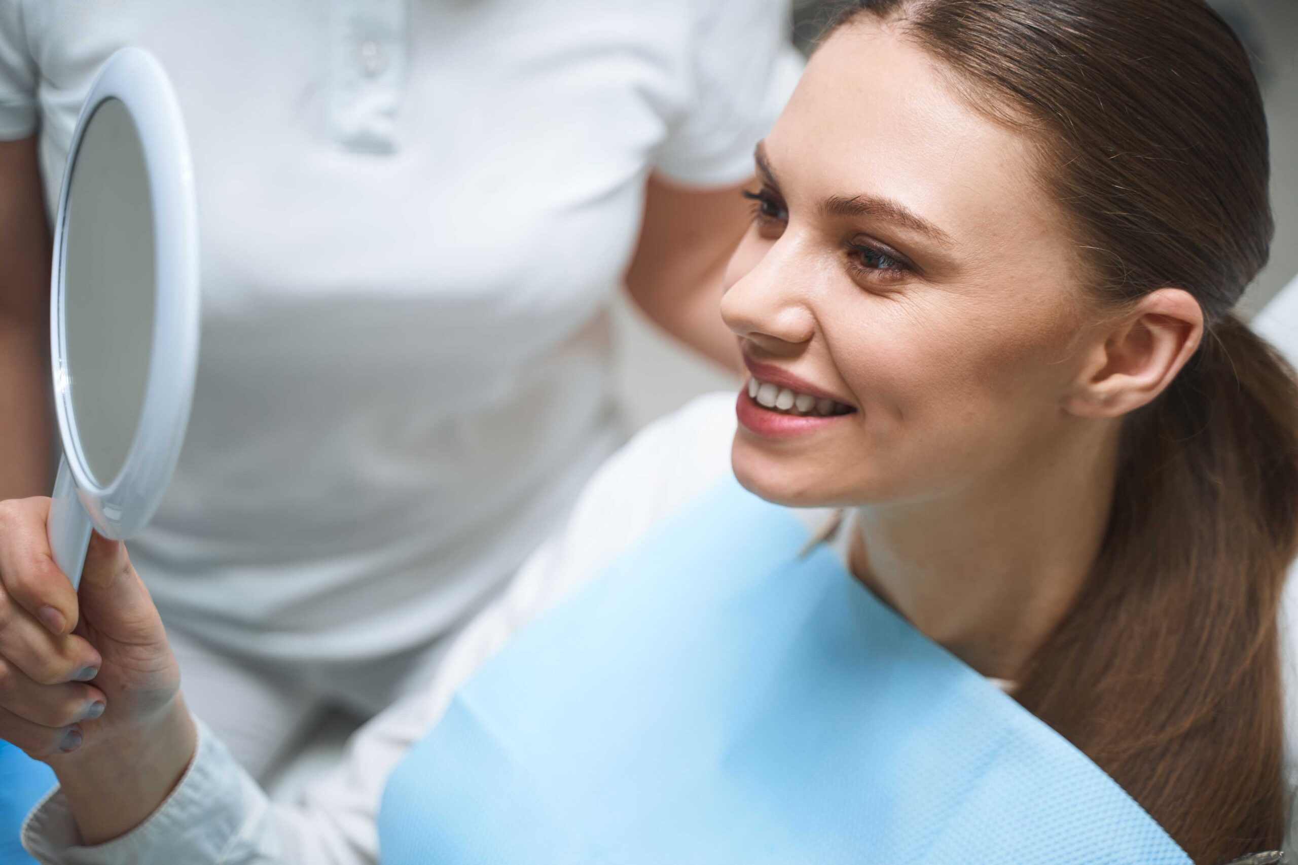 dental-exam-teeth-gums-bite Patient smiling at her smile in a dental mirror.