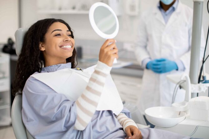 full-mouth-reconstruction-planning Smiling patient checking her smile in a mirror after dental treatment.